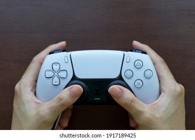 Bangkok, Thailand - February 14, 2021 : Hand Holding Playstation 5 DualSense Wireless Controller On The Wooden Table, New Sony Gaming Console.