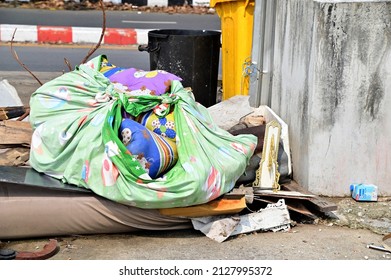 BANGKOK, THAILAND - February 20, 2022 : An Old Quilt In Green And Blue Beside A Pile Of Rubbish On The Edge Of The Footpath.