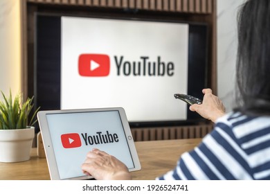 Bangkok, Thailand, February 25, 2021: Youtube Logo, Video Content Social Media App On Ipad Sharing To Tv Screen Background With User Watching Digital Vdo Clip At Home In Living Or Dining Room