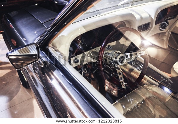 BANGKOK, THAILAND - January 1, 2017: Ford
Mustang interior and wooden steering wheel shot through driver side
window. Classic car dashboard. Illustration of vintage car &
retro car restoration.