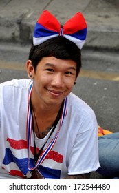 Bangkok, Thailand January 17, 2014::  Cute Thai Youth Wearing Shut Down Bangkok Tee-shirt And A Red, White, And Blue Giant Hair Bow Sitting On Silom Road Selling Souvenirs