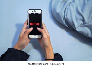 Bangkok, Thailand - January 21, 2019: Woman Hand Holding IPhone Screen Showing Netflix Logo On The Bed.