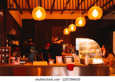 Bangkok, Thailand - January 23, 2022: Busy Staff Preparing Beverage And Coffee To Serve To Customer Inside Local Shop Decorated By Orange Bright Light.