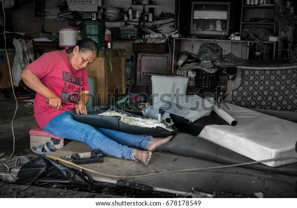 BANGKOK,\
THAILAND - July 1: Underpaid low income migrant worker fixes a\
motorcycle seat. Due to lack of labor protection, women make up\
almost 40% of migrant workers in\
Thailand.