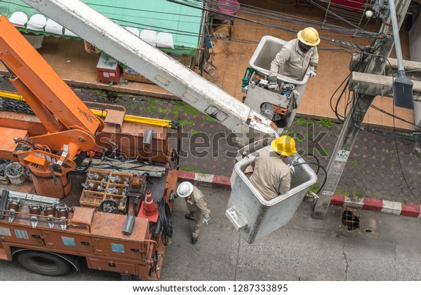 Bangkok, Thailand - July 22, 2018:\
electricians in uniform and helmets repair an street electric pole\
being on aerial work\
platforms.
