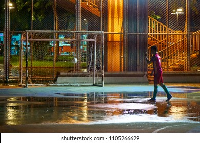 BANGKOK, THAILAND - July 23, 2017: Alone Kid Playing With A Soccer Football Under Evening Rain On Wet Open Air Mini Football Pitch Playground. Street Sport Activity Concept.