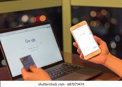 BANGKOK, THAILAND - July 29, 2017: Freelancer Female Using Iphone 7 With Macbook Pro With Google Search Engine On Web Page And Holding Credit Card For Working At Night  From Home