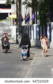 Bangkok, Thailand - June 28, 2015: Arabic Woman In Black Hijab Pushing A Baby Stroller On A Street Near Charoen Krung Rd In Hot Sunlight