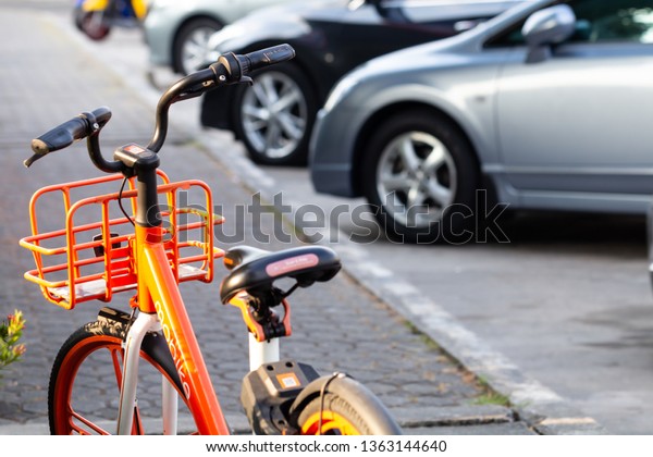 BANGKOK, THAILAND - MARCH 31, 2019: orange\
bicycle in bike sharing project, scan and ride by mobike with car\
parking as background at bangkok,\
thailand