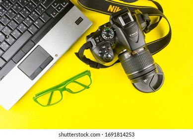 Bangkok, Thailand - March, 31, 2020 : Green Frame Glasses, Notebook Computer And Dslr Nikon D5300 Isolated On Yellow Background.