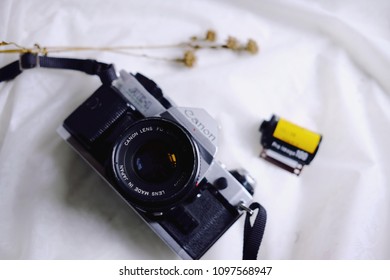 BANGKOK, THAILAND - MAY 05, 2018: Canon AE-1 Program 35mm Film Camera And A Roll Of Kodak ProImage 100 The Professional 135 Color Negative Film With Dry Flowers On White Tablecloth. Copy Space