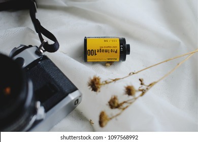 BANGKOK, THAILAND - MAY 05, 2018: Canon AE-1 Program 35mm Film Camera And A Roll Of Kodak ProImage 100 The Professional 135 Color Negative Film With Dry Flowers On White Tablecloth. Copy Space