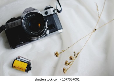 BANGKOK, THAILAND - MAY 05, 2018: Canon AE-1 Program 35mm Film Camera And A Roll Of Kodak ProImage 100 The Professional 135 Color Negative Film With Dry Flowers On White Tablecloth. Copy Space