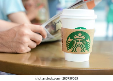 Bangkok, Thailand - May 20, 2015 : Starbucks Coffee Cup On The Table With A Man Reading Newspaper As Background In Starbucks Coffee Shop.