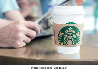 Bangkok, Thailand - May 20, 2015 : Starbucks Coffee Cup On The Table With A Man Reading Newspaper As Background In Starbucks Coffee Shop.