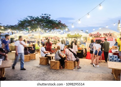 BANGKOK, THAILAND - May 2018 - People Sitting On Wooden Chairs,walking,eating And Buying Food At Street Food Market Festival In A Park. Market Stalls. Shopping. Outdoor Market. Food Event. Food Fair. 