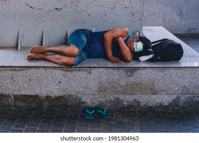 BANGKOK, THAILAND - MAY 2021: asian thai homeless sleeping on pavement, wearing hygiene face mask covering eyes. Protective mask due to COVID-19 coronavirus. Poor man taking nap outdoors. 