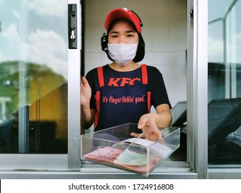 Bangkok, Thailand - May 7, 2020 : KFC fast food cashier in drive thru service waring hygiene face mask to protect coronavirus pandemic or covid-19 virus outbreak is giving money change to customer.
