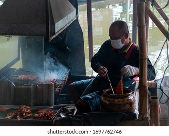 Bangkok, Thailand - November 2, 2019: Older Asian Man Cooking Some Pork Brochettes At A Street Market