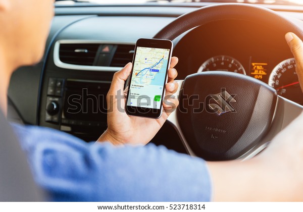 Bangkok, Thailand - November 23, 2016: man\
using maps application on iphone and driving suzuki swift car,\
navigation maps ios app is available on app\
store