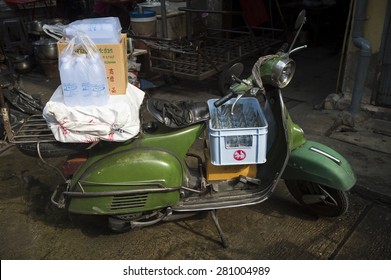 BANGKOK, THAILAND - OCTOBER 27, 2014: A Traditional Old Green Scooter Loaded With Bags Stands Parked On A Dark Alley.