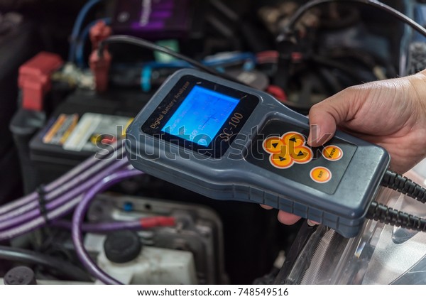 Bangkok, Thailand - October 7, 2017 : Unidentified\
car mechanic or serviceman checking a car battery by Digital\
Battery Analyser tools for fix and repair problem at car garage or\
repair shop
