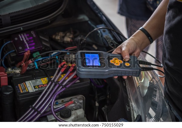 Bangkok, Thailand - October 7, 2017 : Unidentified\
car mechanic or serviceman checking a car battery by Digital\
Battery Analyser tools for fix and repair problem at car garage or\
repair shop