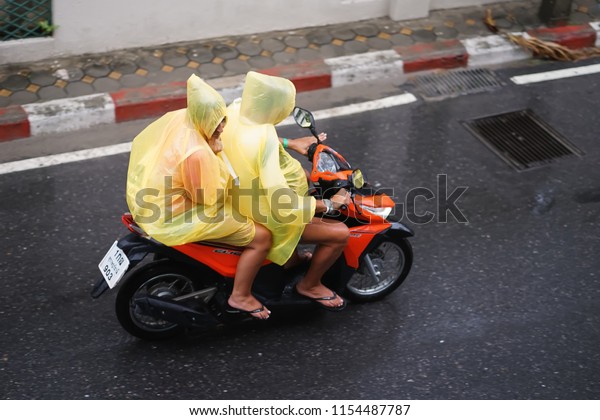 In Bangkok, Thailand, on August 12, 2018, people\
were driving a motorbike in the rain, with a yellow raincoat on the\
road.