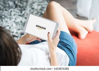 Bangkok/Thailand - June 8 2019 : A Woman Lying Down Relaxing On A Day Bed  While Logging In To Amazon Application On Tablet Computer. Online Shopping, Holidays, E-commerce, Technology Lifestyle.