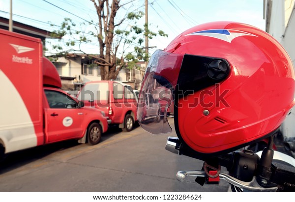 Bangkok/Thailand -\
November 7,2018 : A fast delivery service of Thailand Post, seeing\
a red helmet of postman biker as a foreground and a red white post\
truck as background.\
