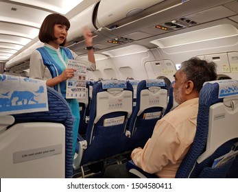 Bangkok,Thailand-Circa August 2019: Cabin Crew Of Bangkok Airways Stands Showing The Safety Instruction Card In Hand To Passenger Who Sits At The Emergency Exit Doorway.