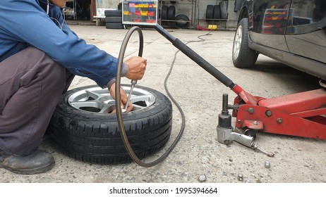 Bangkok,Thailand-June 15,2021 : Male Auto Mechanic Inflate Car Tires At Wheel In Auto Repair Shop.Tire Lying On The Floor.Maintenance Service Concept