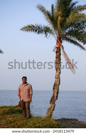 Bangladeshi young traveler exploring a riverside area standing beside date palm tree 
