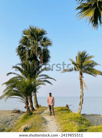Bangladeshi young traveler exploring a riverside area standing beside date palm tree 