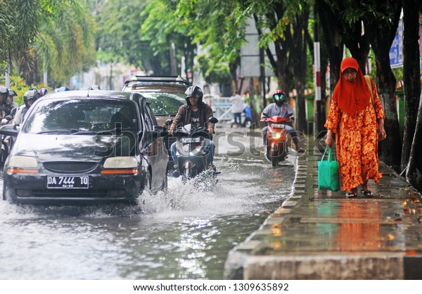 Banjarmasin,\
South Kalimantan, Indonesia, 11 - February 2019: It was raining\
several hours in the flooded city of Banjarmasin, seen by several\
motorbike riders and cars passing the\
flood.