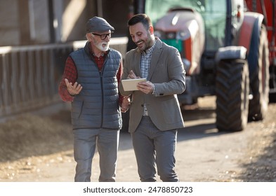 Bank agent and senior farmer talking about business and looking at tablet in front of tractor on cattle ranch - Powered by Shutterstock