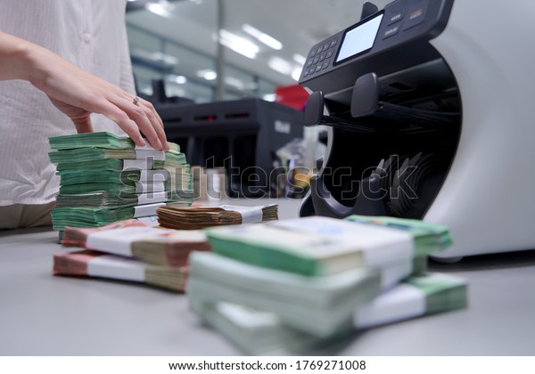 Bank employees using money counting machine while\
sorting and counting paper banknotes inside bank vault. Large\
amounts of money in the\
bank