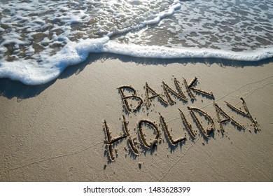 Bank Holiday Message Handwritten On The Smooth Sand Of An Empty Beach With Oncoming Wave