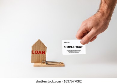 Bank Investments And Mortgages. Male Hand Holds Bank Card Near The Trap With A Cardboard Schematic House. Text LOAN