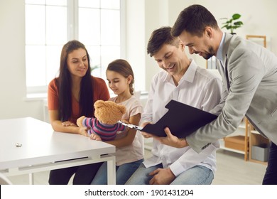 Bank Manager Talking To Clients. Happy Young Family Meeting With Financial Advisor Or Real Estate Agent. Couple With Child Reading Terms Of Mortgage Loan, Rental Agreement Or House Purchase Contract