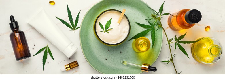 Bank of medicinal cream with CBD oil, bottle of cannabis oil, capsules, on a green plate. Flat lay, top view. Banner