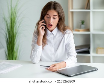 Bank Operation. Shocked Woman. Mobile Communication. Arguing Office Lady Holding Credit Card Talking Smartphone Sitting Work Desk In Light Room Interior.