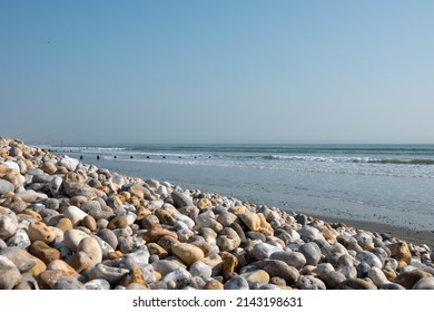 bank of pebbles with the sea and beach in the background