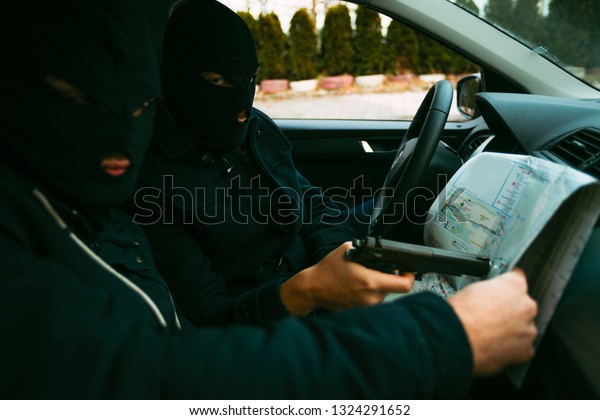 Bank robbers with their masks on pointing at the\
map prepared for robbing the bank,sitting in the car and waiting\
for the right time to rob.