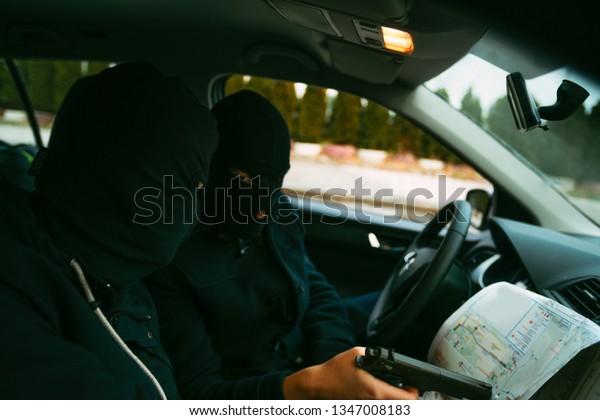 Bank robbers with their masks on pointing at the\
map prepared for robbing the bank,sitting in the car and waiting\
for the right time to rob.