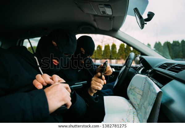 Bank robbers with their masks on pointing at the
map prepared for robbing the bank,sitting in the car and waiting
for the right time to rob.