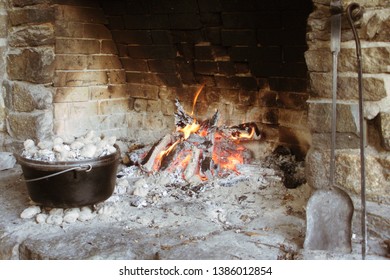 A Banked Fire In A Brick Fireplace Next To A Dutch Oven Surrounded By Coals And Fire Tending Tools To The Side