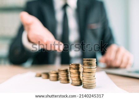 Banker offering financial loan, closeup of white collar business person in office with stacked coins on the desk, selective focus