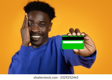 Banking concept. Thilled happy young black man wearing basic casual sweater holding in hand credit bank card and touching face, isolated on yellow colour background, studio shot, copy space