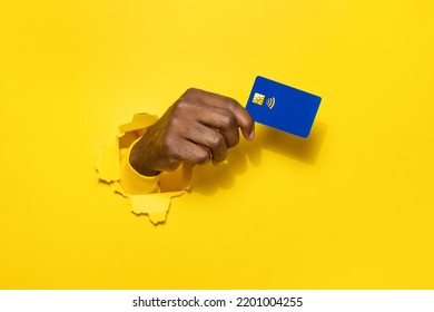 Banking Services. African American Male Hand Holding Plastic Credit Card Through The Torn Yellow Studio Background, Copy Space, Cutout